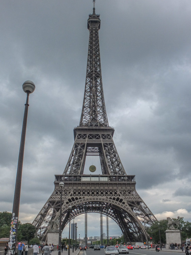 a tall metal tower with a cloudy sky with Eiffel Tower in the background