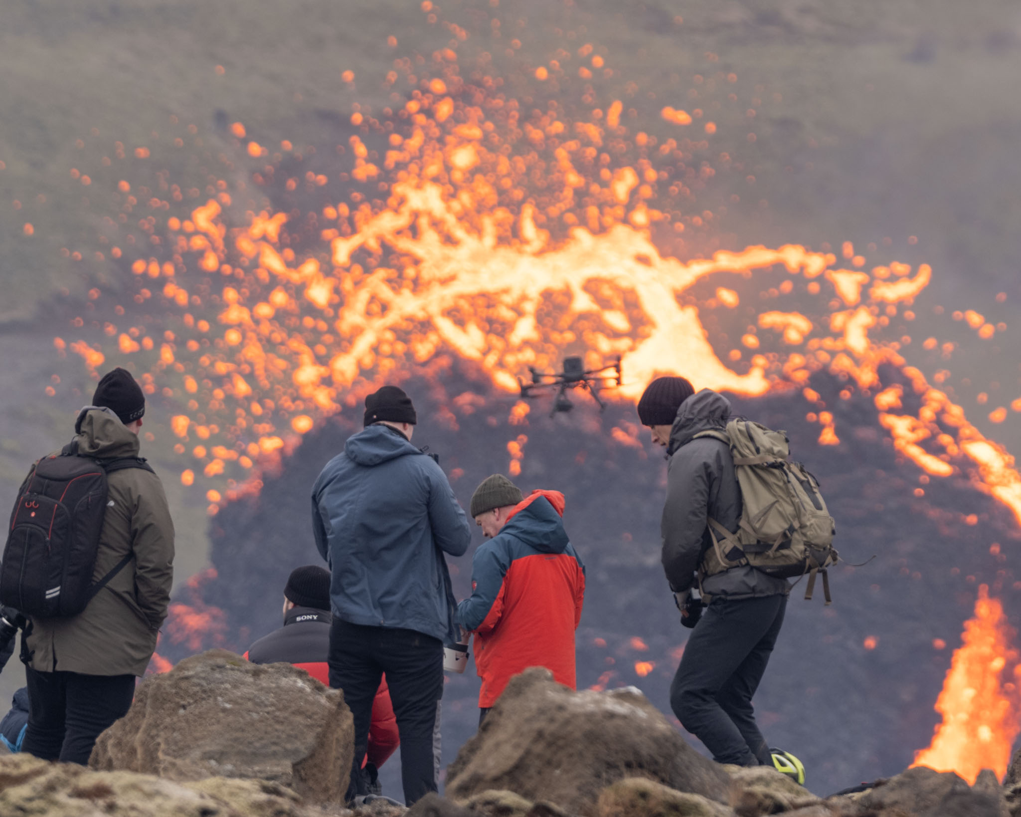 a group of people looking at a drone in front of a volcano