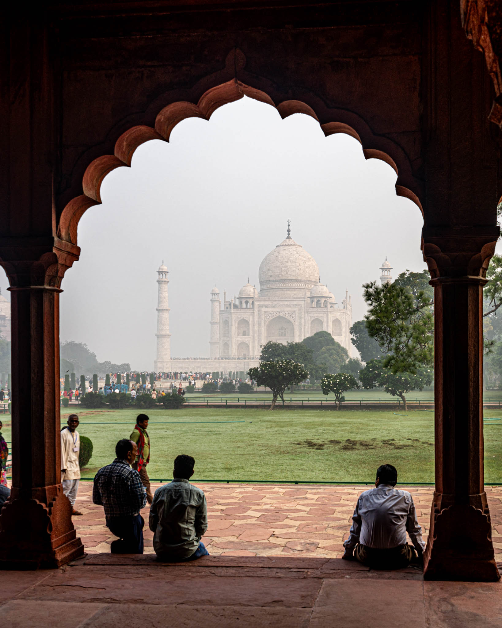 people sitting on a brick walkway looking at a large building with Taj Mahal in the background