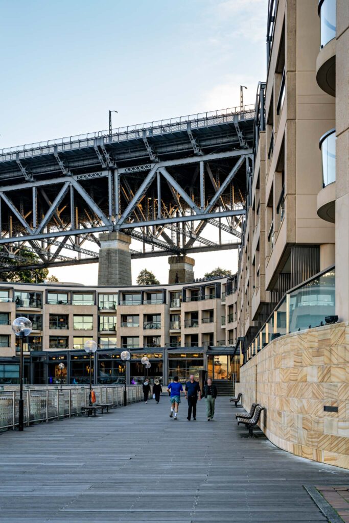 a group of people walking on a walkway under a bridge