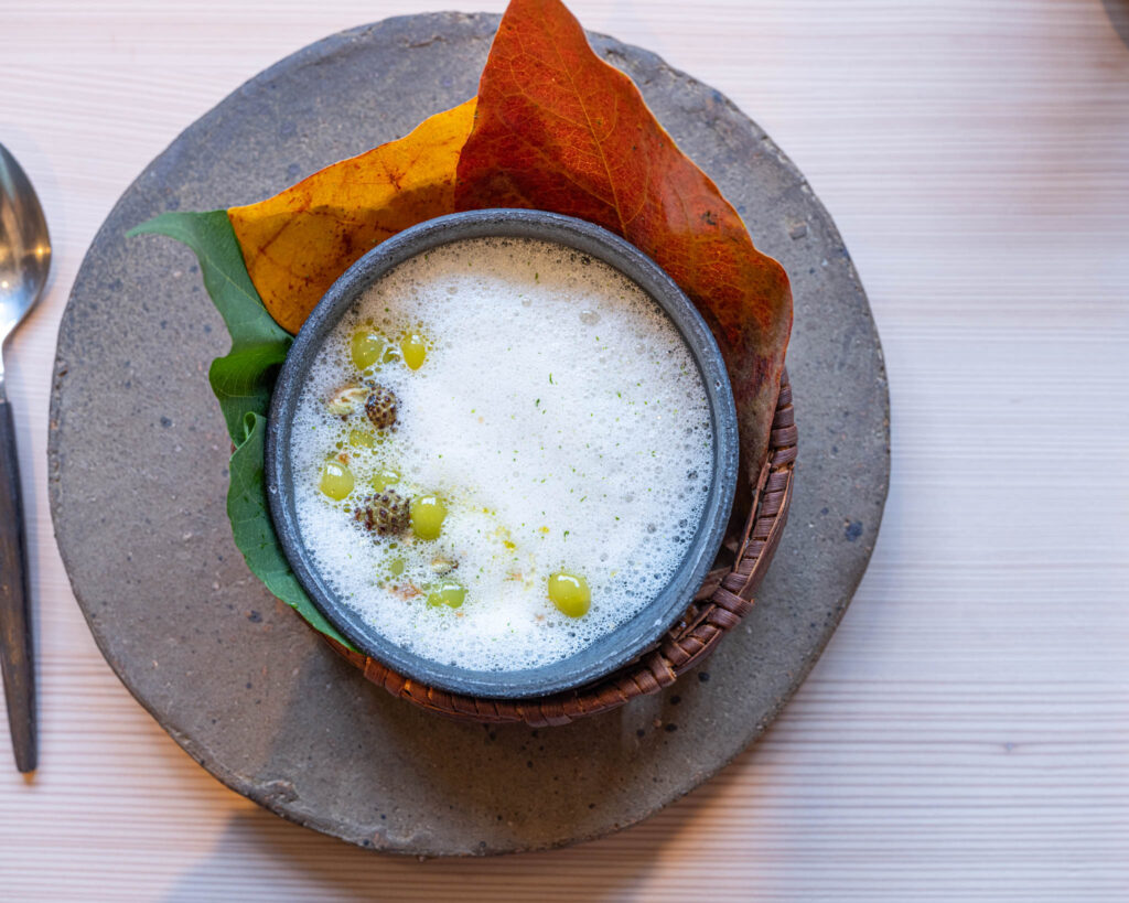 a bowl of white liquid with yellow and green seeds on top of a leaf