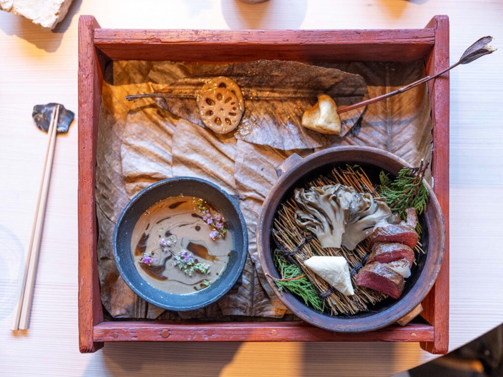 a bowl of soup and meat in a wooden tray