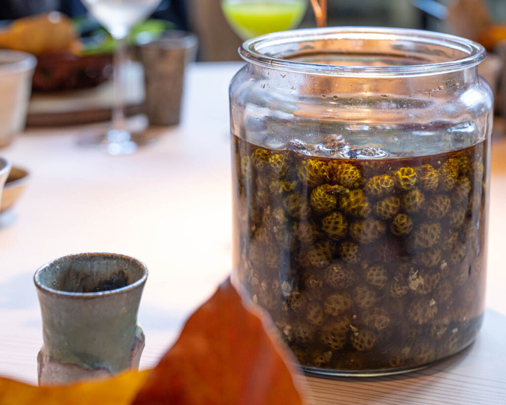 a jar of brown liquid with green berries in it