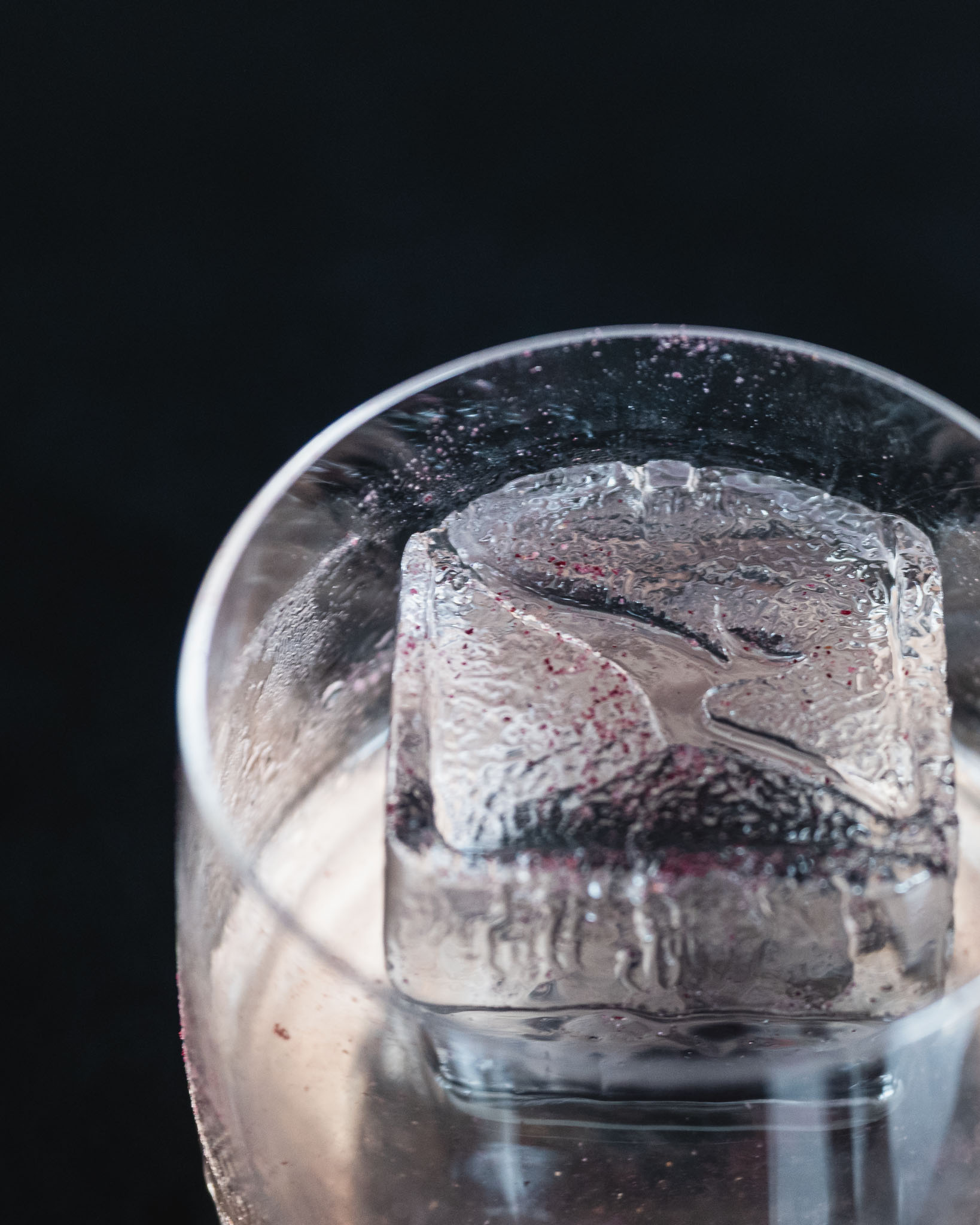 a glass with a clear liquid and a ice cube in it
